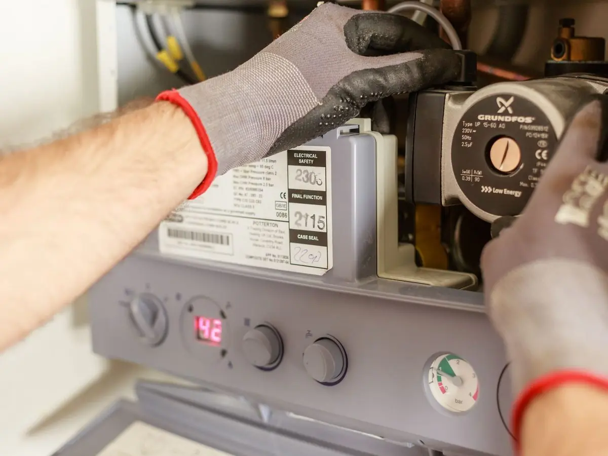 Gloved hands working on the controls of a wall-mounted heating unit