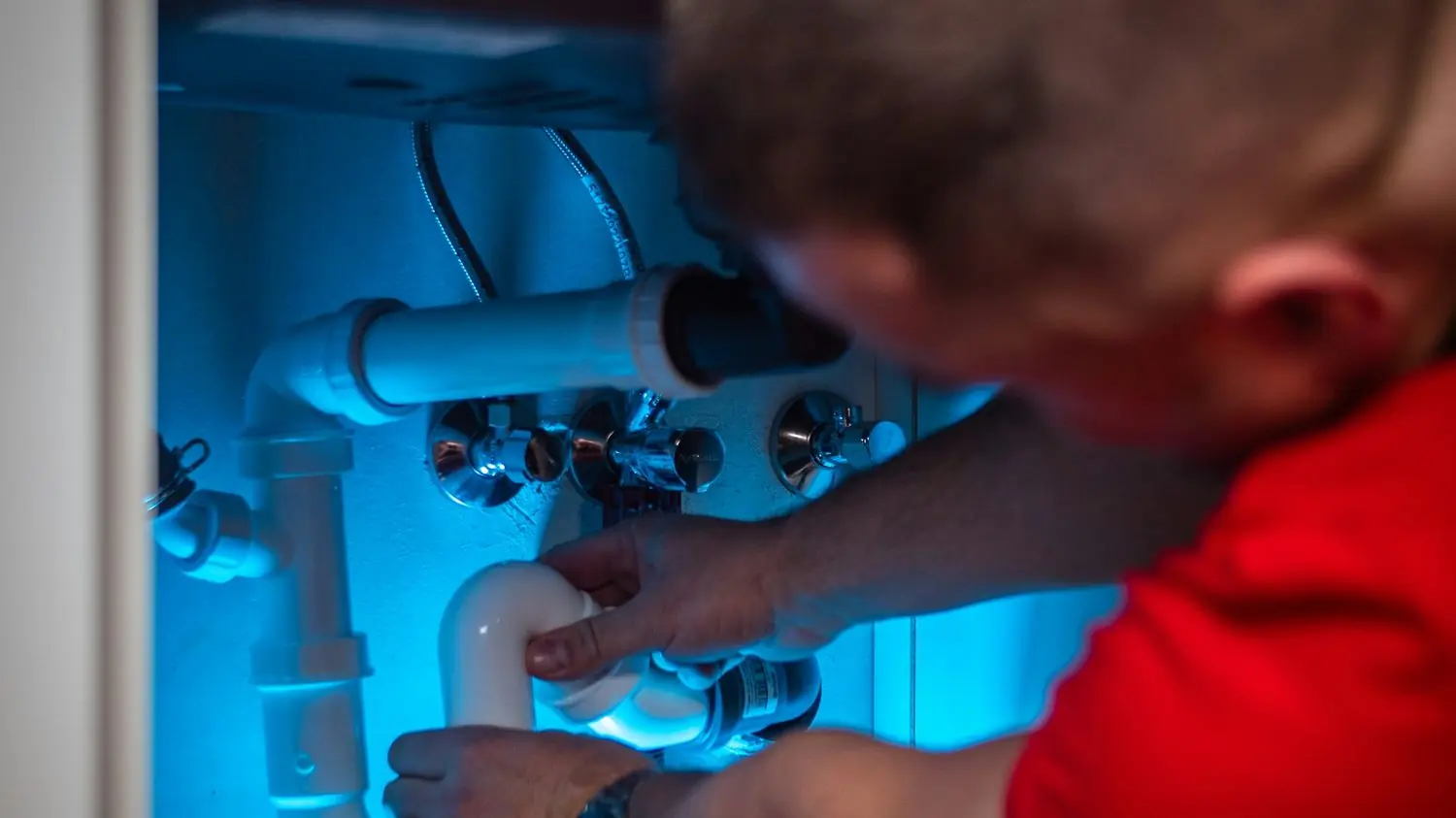 Plumber reaching into a cabinet to work on pipes