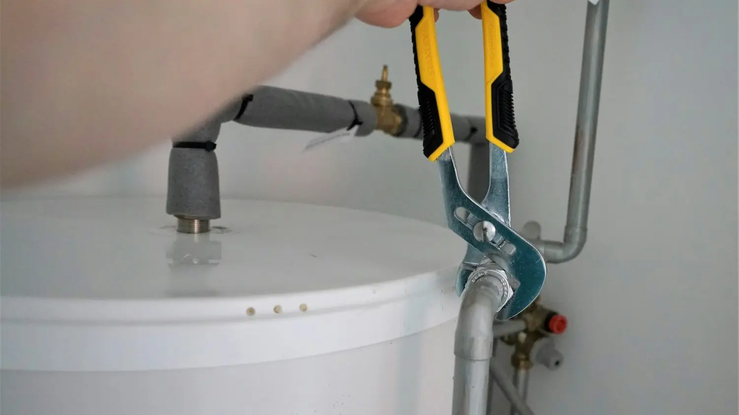 Plumber tightening a fitting on top of a tank water heater