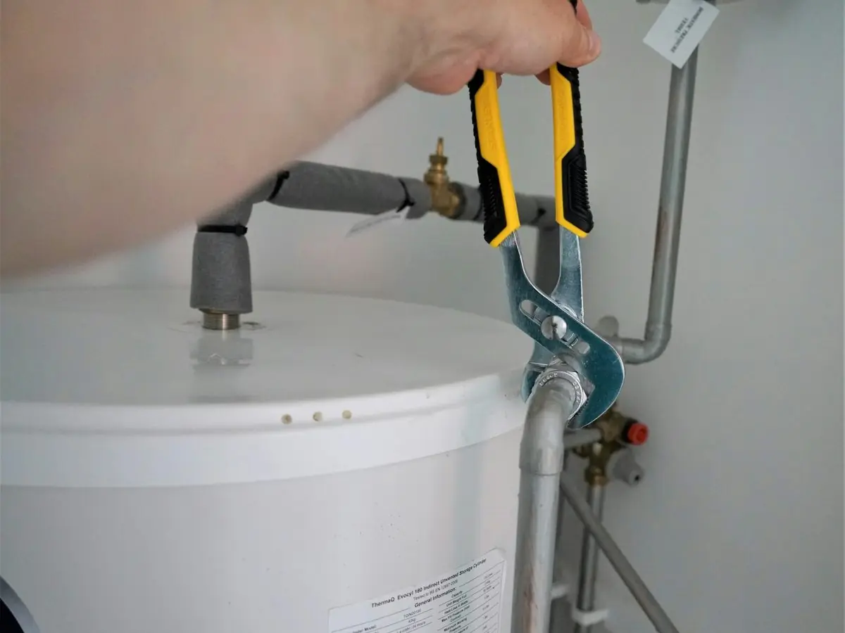 Plumber tightening a fitting on top of a tank water heater
