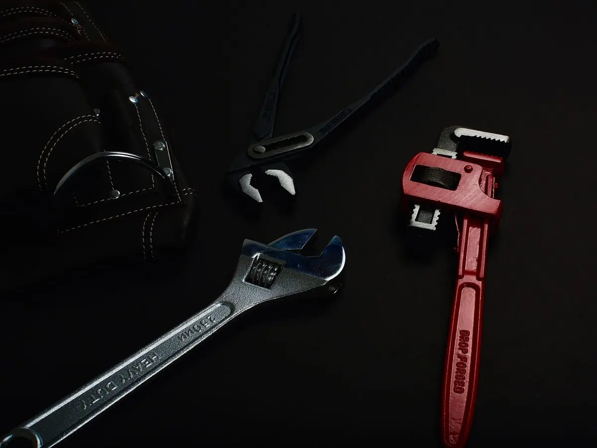 Plumbing wrenches and pliers on a dark bench
